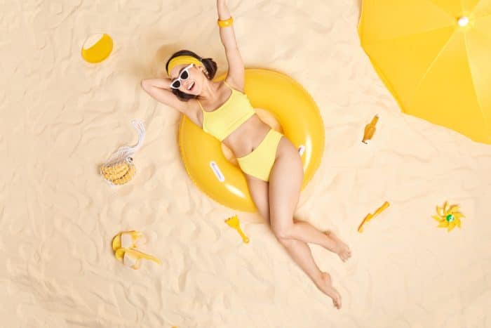 Young women in a yellow two-piece swimsuit, reclined on a yellow ring-shaped floatable reclined in the sand.