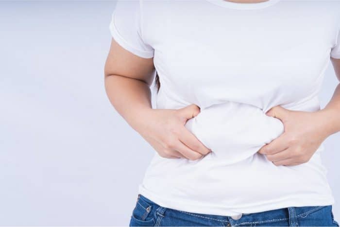 Caucasian male in white t-shirt gripping a roll of belly fat in two hands.