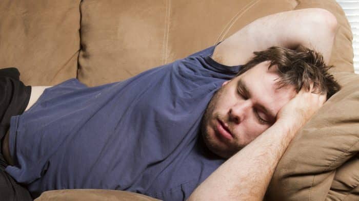 White male in blue t-shirt sleeping on a sofa.