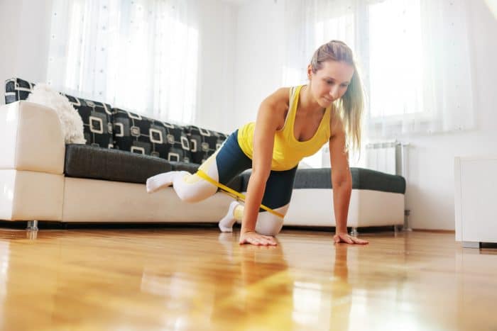 Woman is doing an exercise holding herself above the floor with a band holding her legs together as she stretches against it