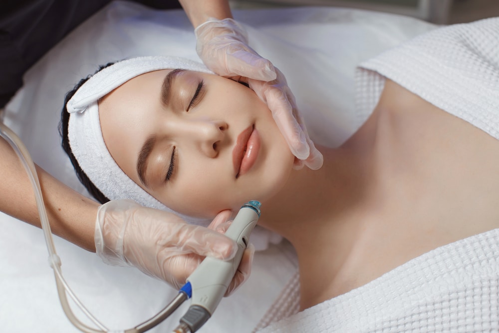 A woman with clear skin has a device firing light placed near her skin by a gloved hand