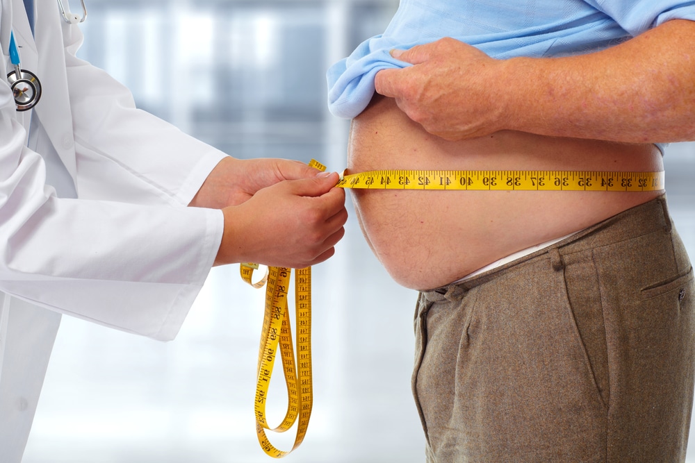 A man with a huge stomach has his waist measured by a doctor with a tape measure