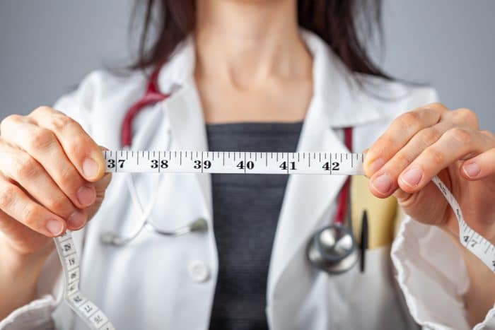 Woman in lab coat holds out measuring tape between her hands