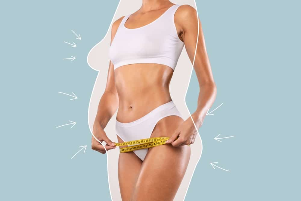 Woman stands in her underwear holding a tape measure in her hands