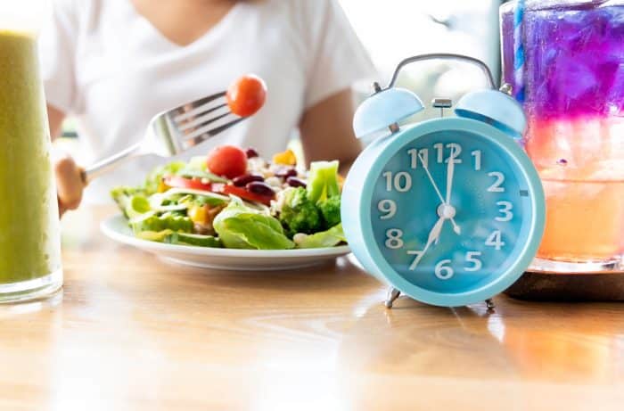 An out of sight person holds up a cherry tomato on a fork above a plate of greens