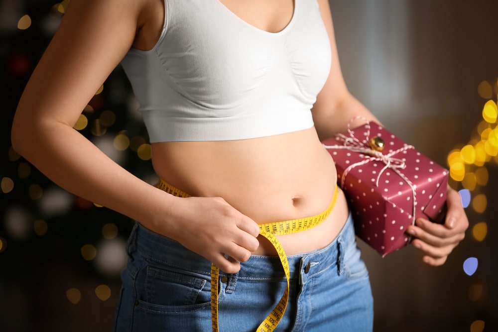 Thin woman with bare midriff measuring her waist with a measuring tape.