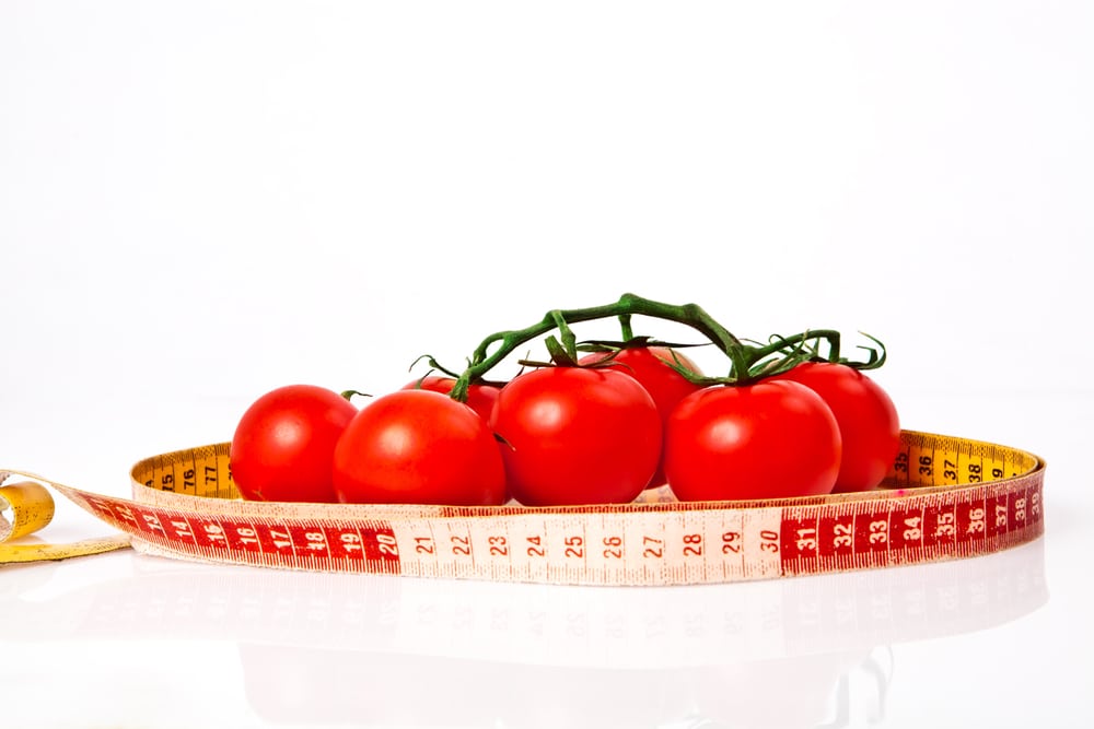 Bright red tomatoes surrounded by a measuring tape wrapped around the bunch.