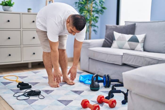 Man stretching on workout mat near weights in his living room