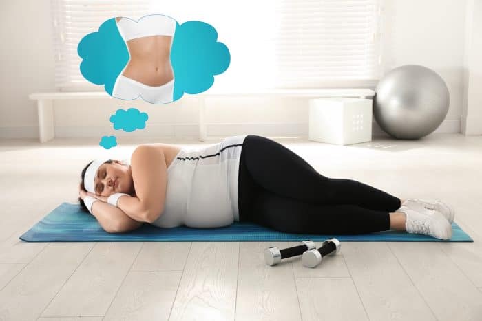 Woman sleeping on workout mat dreaming of weight loss and toned abs