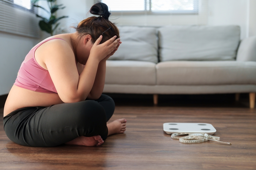 woman sitting next to scale with hands covering face