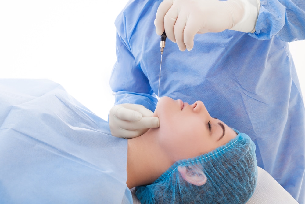 Doctor applying laser lipolysis treatment to woman's neck while she's lying on table.