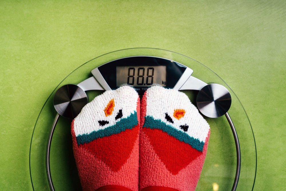 Two feet clad in red, green, and white holiday-themed socks standing on a digital scale.