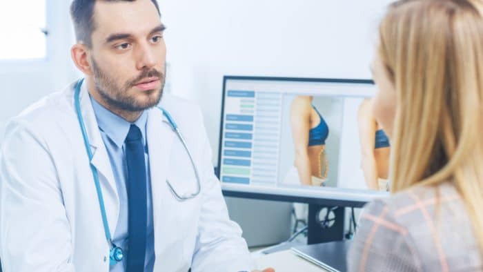 Woman speaking to male doctor about laser lipolysis treatment as they analyze options on computer screen