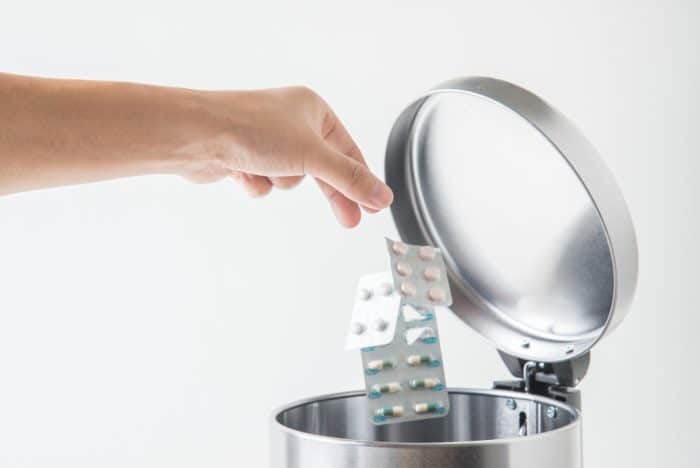Hand throwing medicine in garbage can.