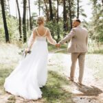 A married couple standing together in a forest, holding hands.