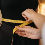 A person uses a yellow tape measure to gauge someone's waist