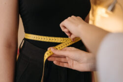 A person uses a yellow tape measure to gauge someone's waist