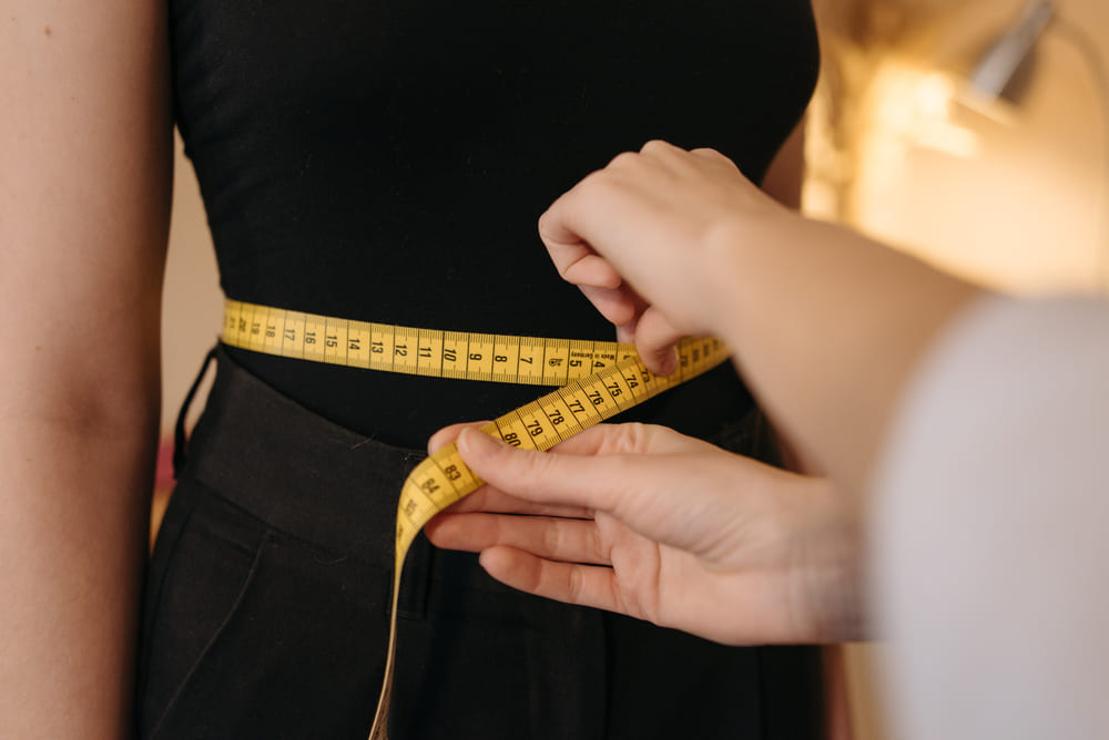 A person uses a yellow tape measure to gauge someone's waist